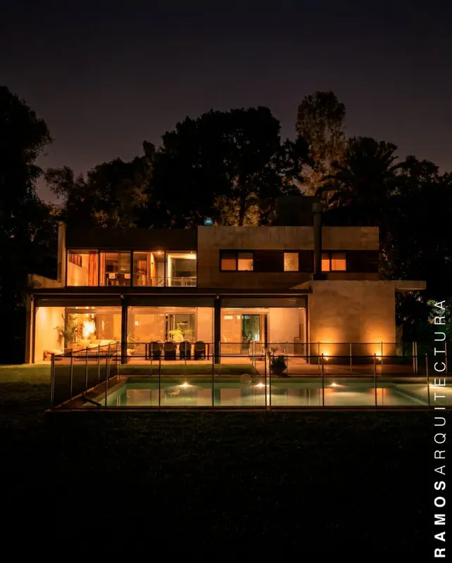 Casa de hormigón con pileta iluminada de noche - Ramos Arquitectura